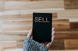 a person holding up a black book with the word sell written on it
