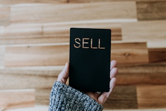 a person holding up a black book with the word sell written on it
