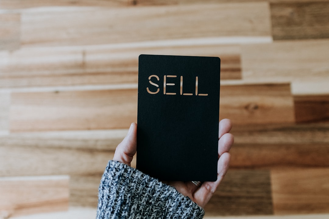 a person holding up a black book with the word sell written on it