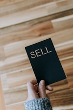 a person holding a black book with the word sell written on it