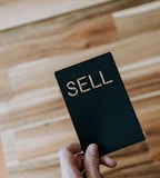 a person holding a black book with the word sell written on it