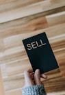 a person holding a black book with the word sell written on it