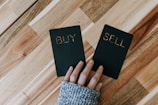 a person holding two small black books with the words buy and sell on them