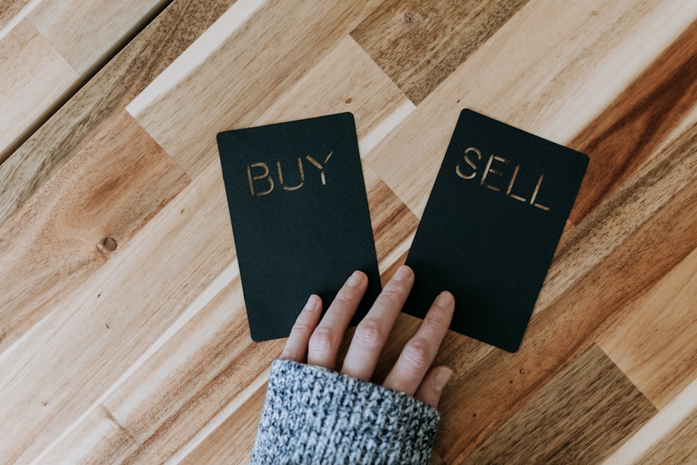 a person holding two small black books with the words buy and sell on them