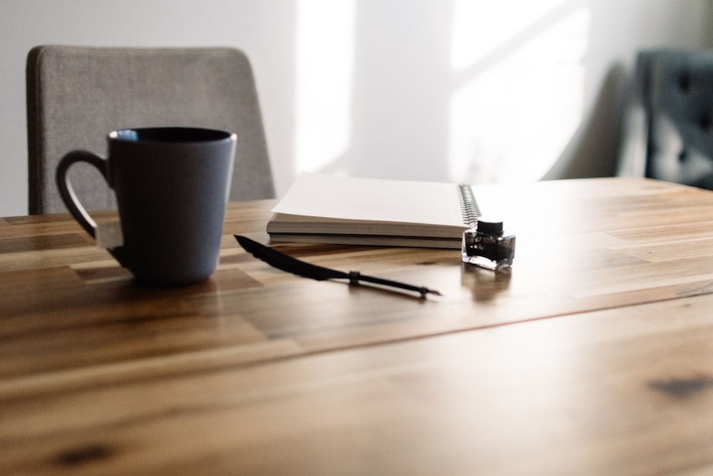 a table with a notebook, pen and a cup of coffee