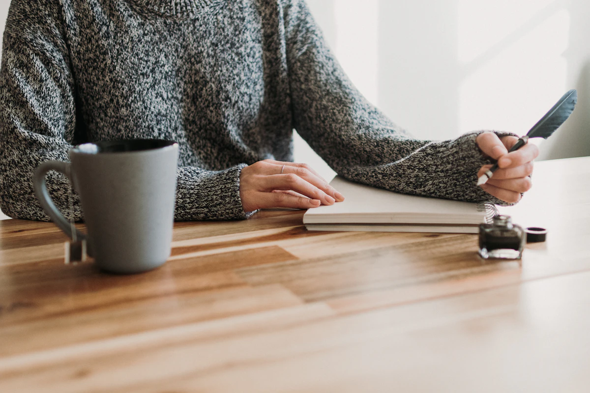 Woman sitting at a table writing in a notebook with a cup of coffee — beginning a personal development self-assessment
