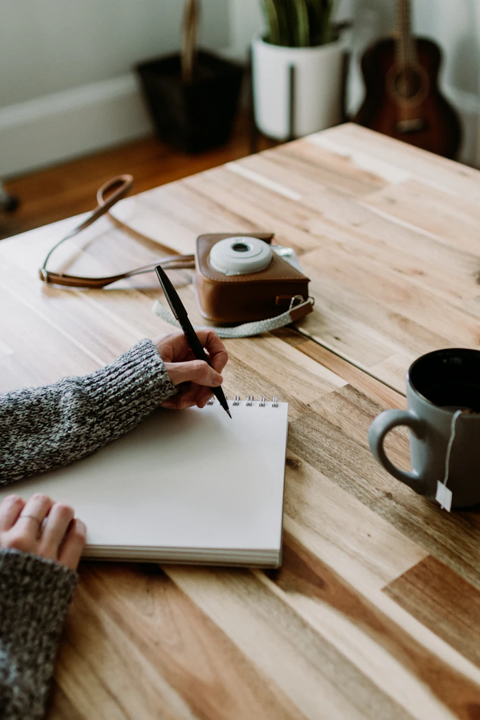 Hands writing in a guided journal beside a cup of tea