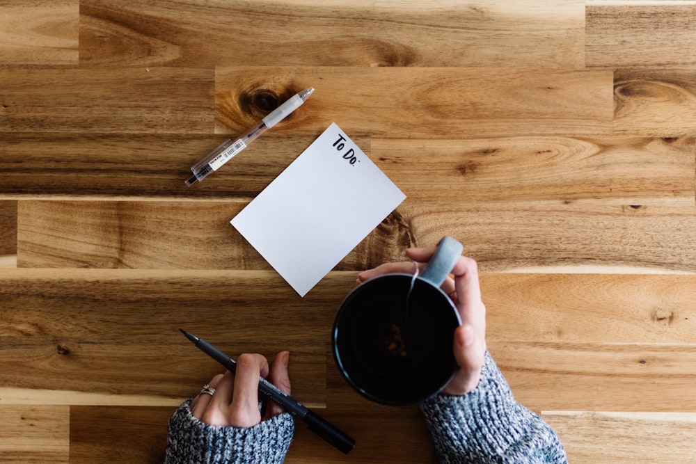 a person writing on a piece of paper next to a cup of coffee