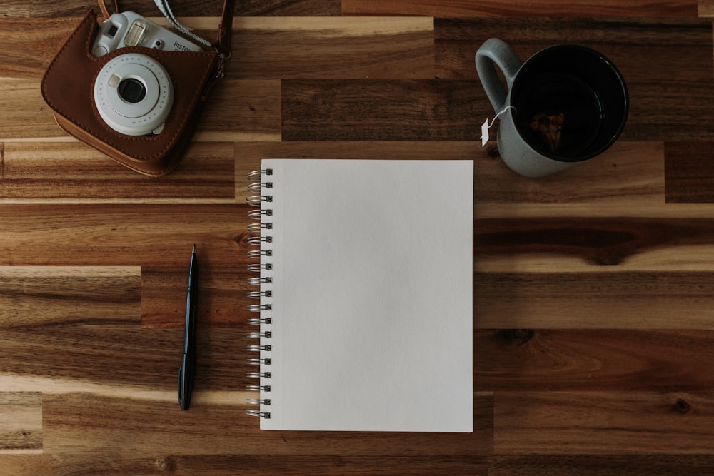 a notepad, pen, camera and a cup of coffee on a wooden table