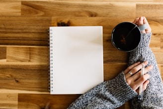 a woman holding a cup of coffee next to a notepad