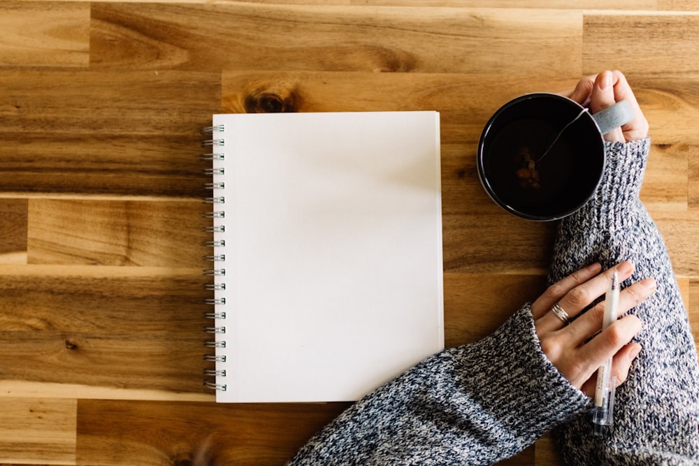a woman holding a cup of coffee next to a notepad