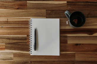 a notepad, pen, and cup of coffee on a wooden table