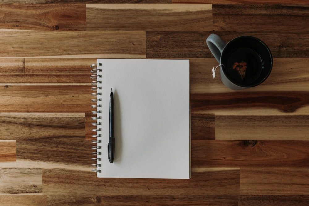 메모장, 펜, 나무 테이블 위의 커피 한 잔