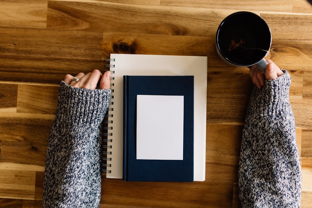 a person holding a cup of coffee next to a notebook