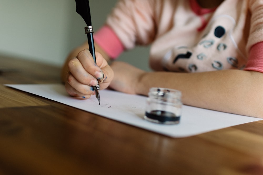 a girl writing on a piece of paper with a pen