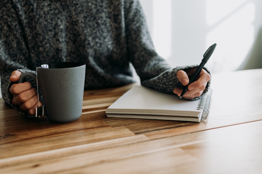 a person holding a pen and writing on a notebook