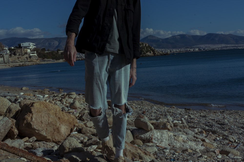 a man standing on a rocky beach next to a body of water