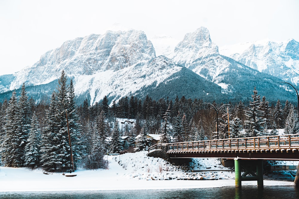 uma ponte sobre um corpo de água com montanhas cobertas de neve ao fundo