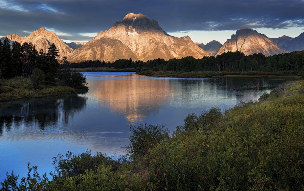 a lake surrounded by mountains under a cloudy sky