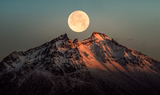 a full moon rising over a snowy mountain