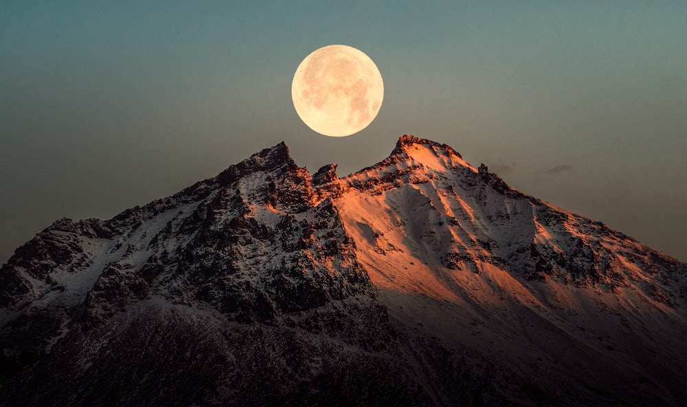 a full moon rising over a snowy mountain