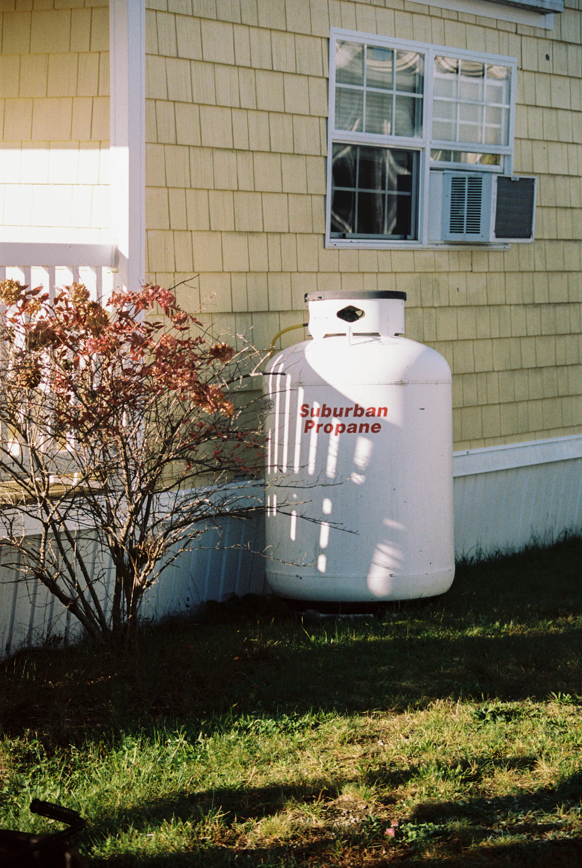 White residential propane tank on the grass beside a house