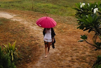 a woman walking down a dirt path with a pink umbrella