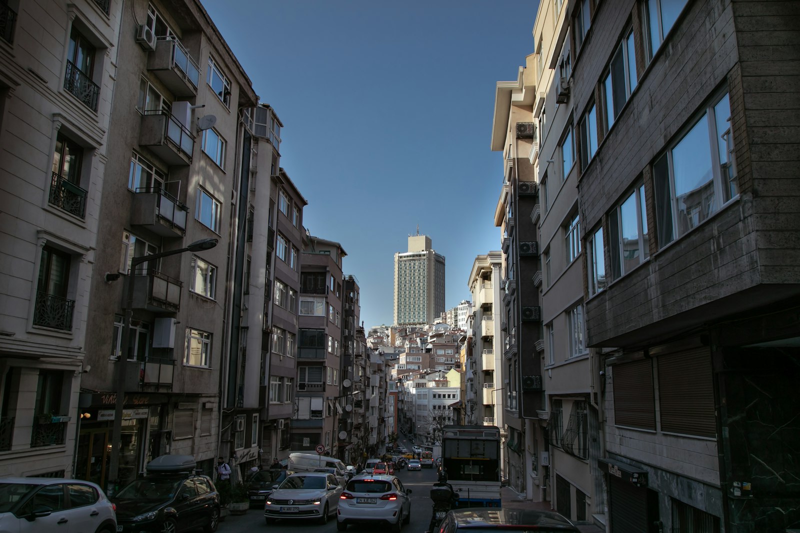Yokuş bir sokağın iki yanında sıralanan apartmanlar ve uzakta yüksek bir bina