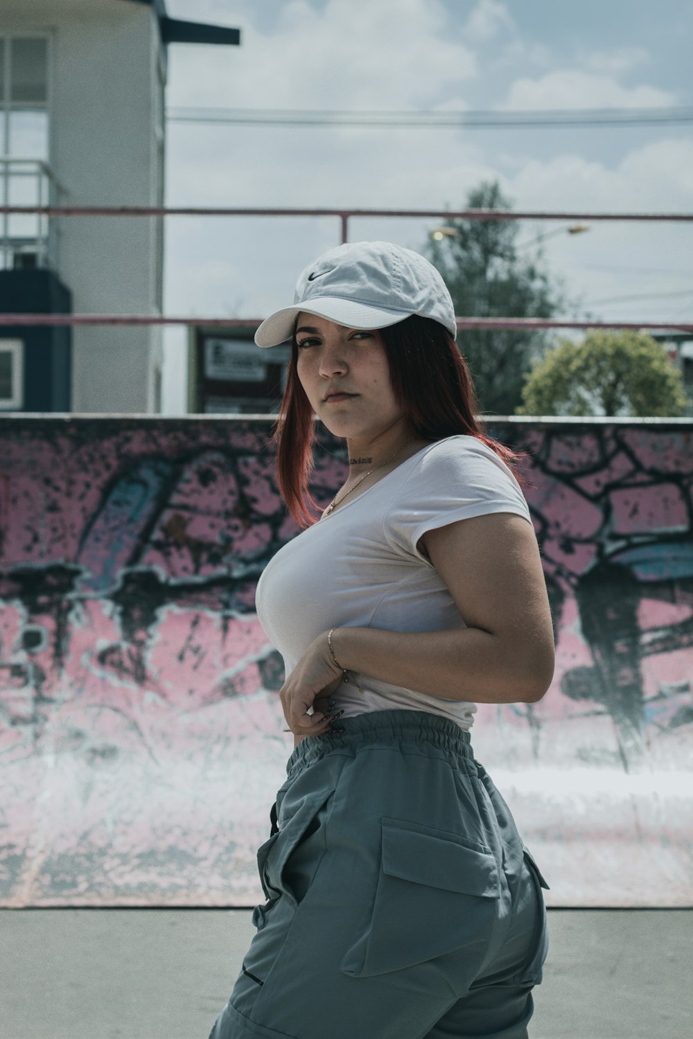 a woman in a white shirt and cap is standing in front of a skateboard