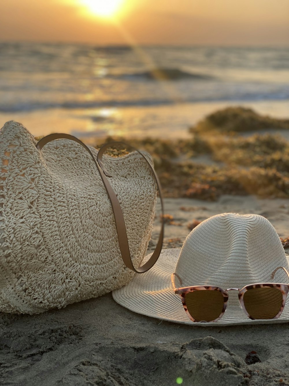 a hat, sunglasses and a straw bag on the beach