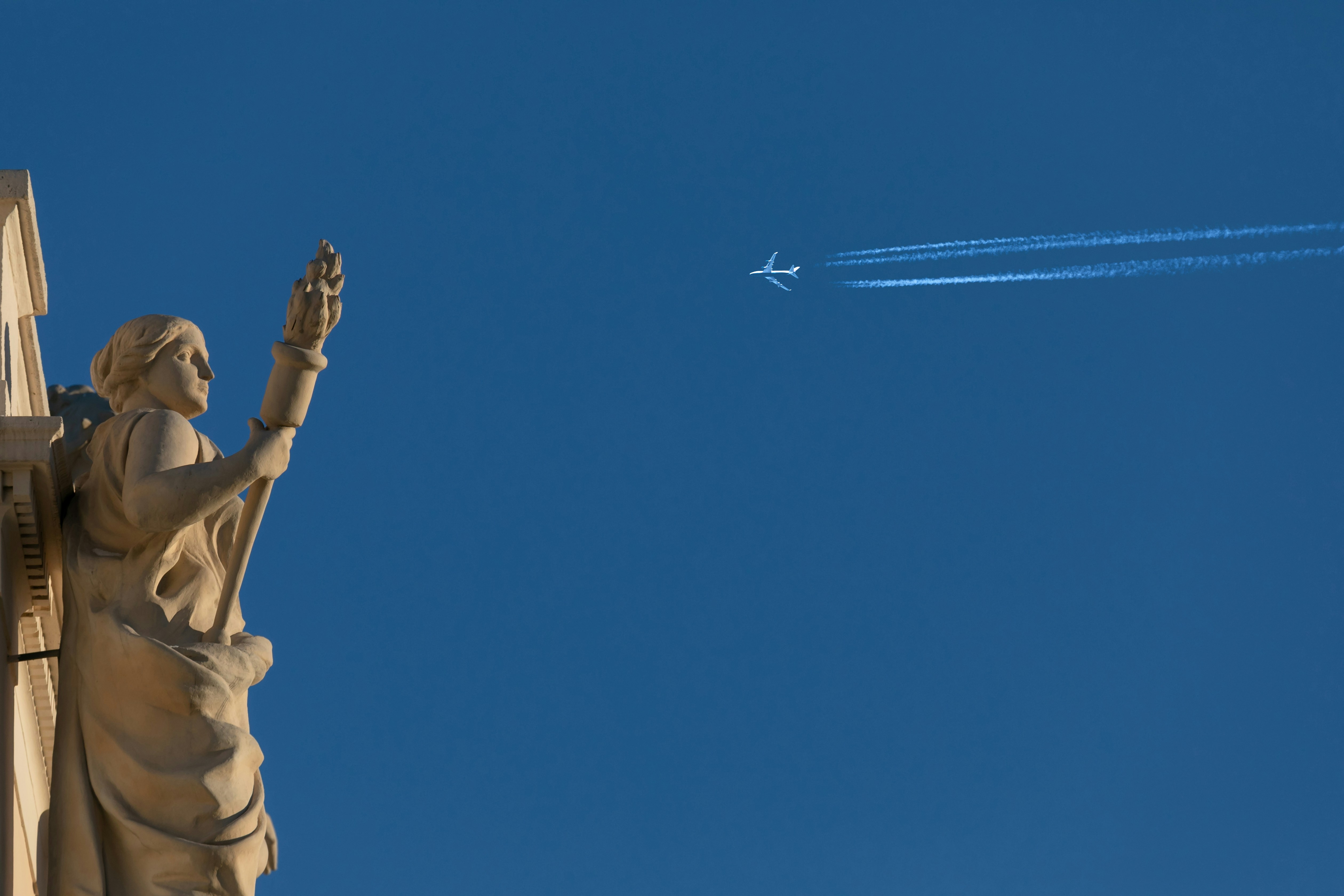 a jet flying in the sky behind a statue