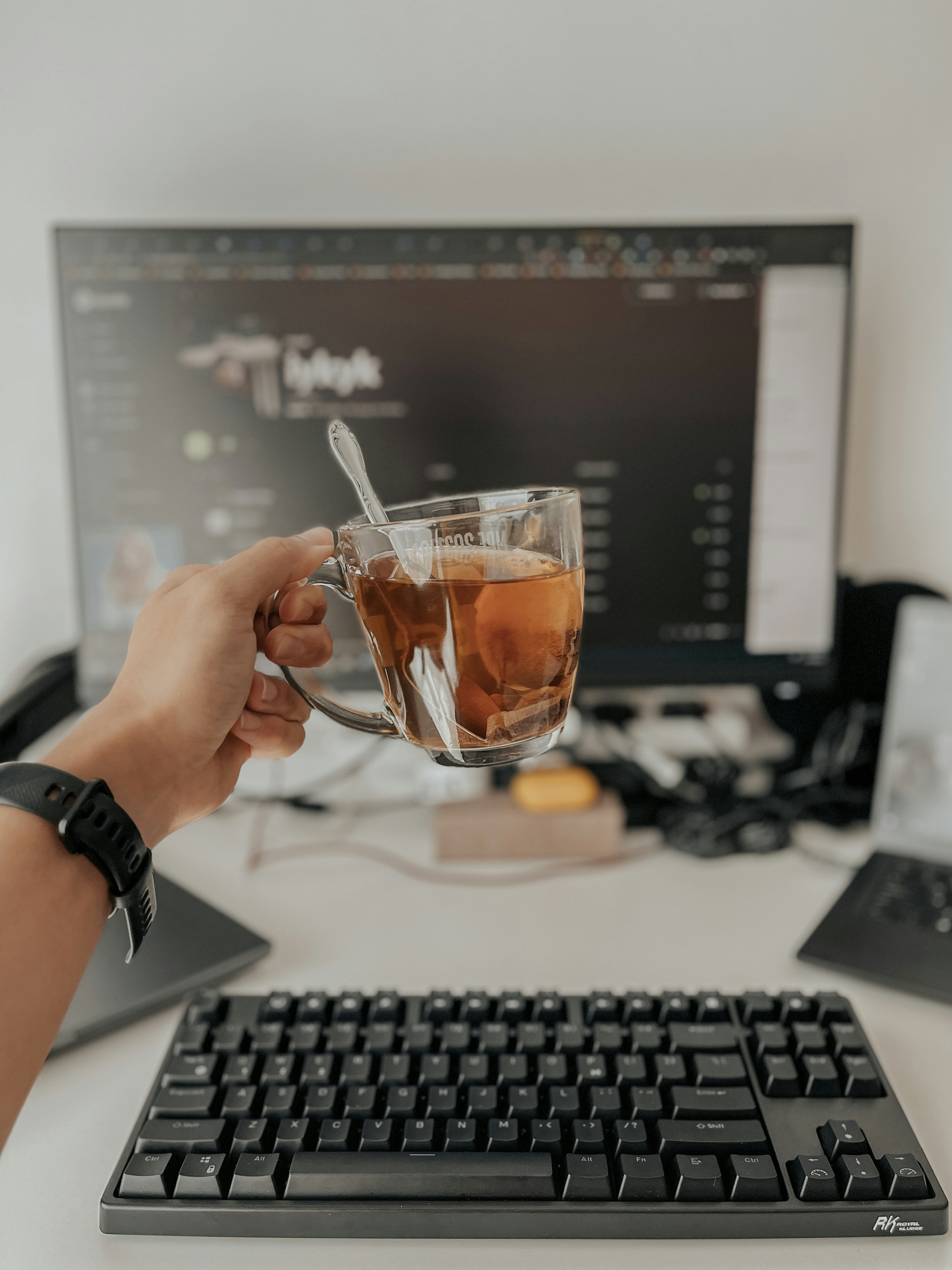 a person holding a glass of tea in front of a computer