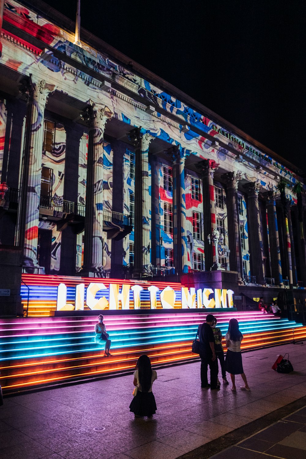 people standing outside of a building lit up at night