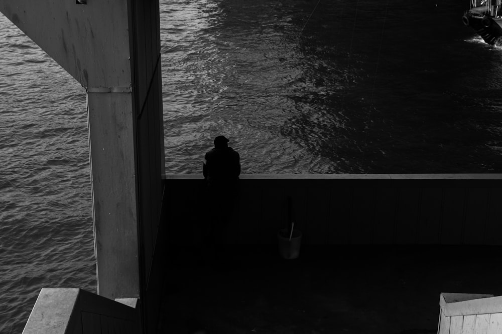 a black and white photo of a person sitting on a dock