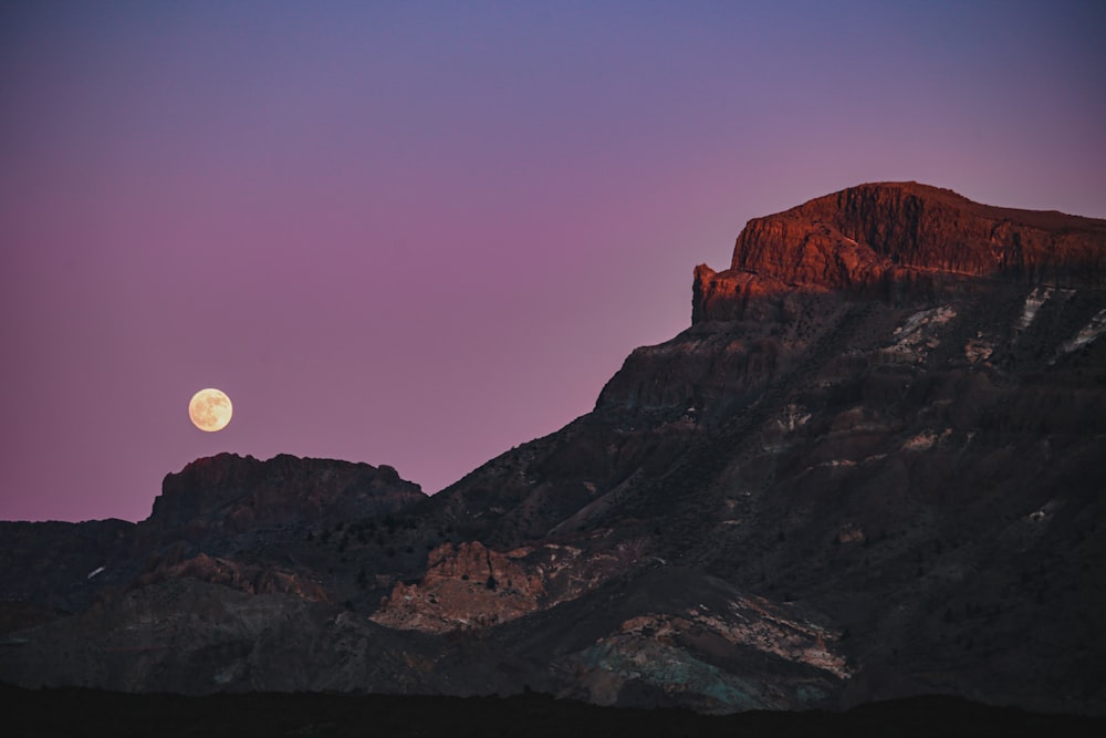 the moon is setting over a mountain range