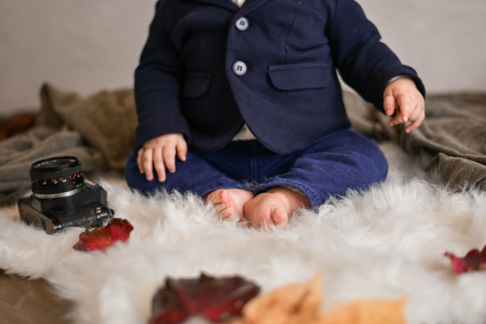 a baby sitting on a white rug with a camera