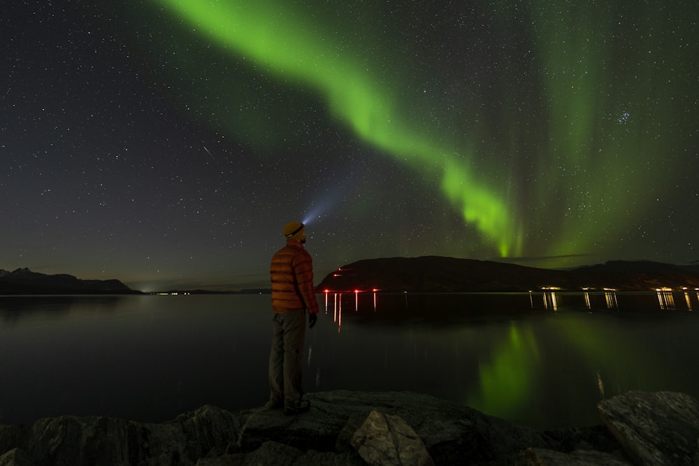 a man standing on a rock looking at the aurora lights