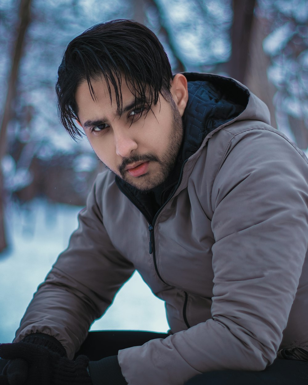 a man with black hair sitting in the snow