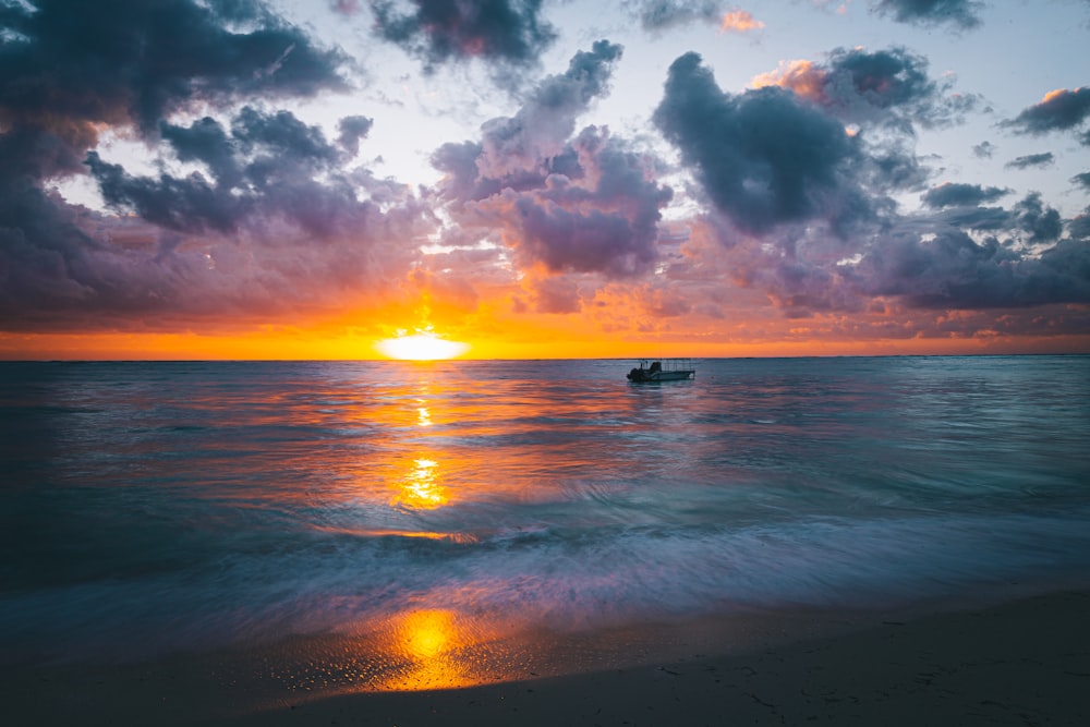 a boat on the water at sunset with clouds in the sky