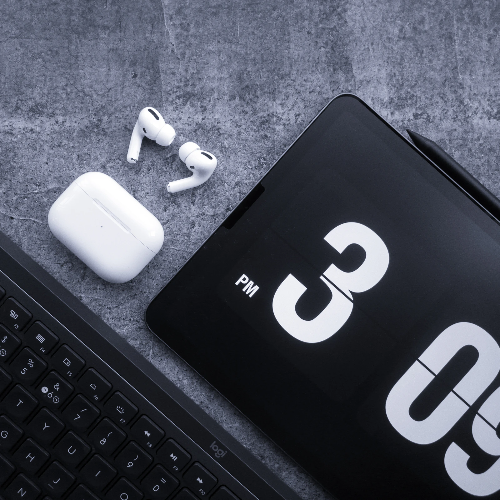 Wireless earbuds, tablet and keyboard arranged in a clean technology flat lay