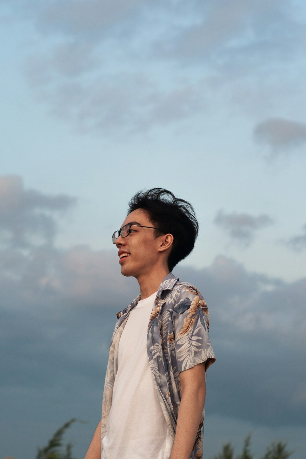 a man with glasses standing in front of a cloudy sky