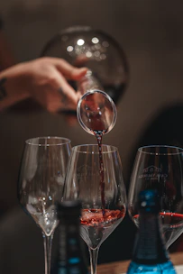 Close-up of a bartender pouring a rich red wine into a crystal glass against a backdrop of glowing candles.