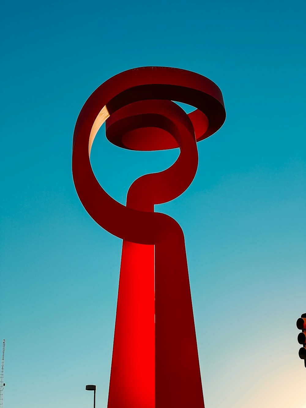 uma escultura vermelha alta sentada ao lado de um semáforo