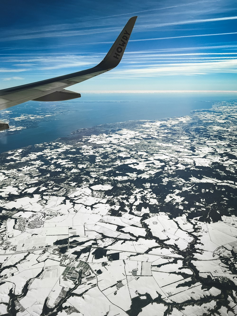 a view of the wing of an airplane flying over a frozen lake