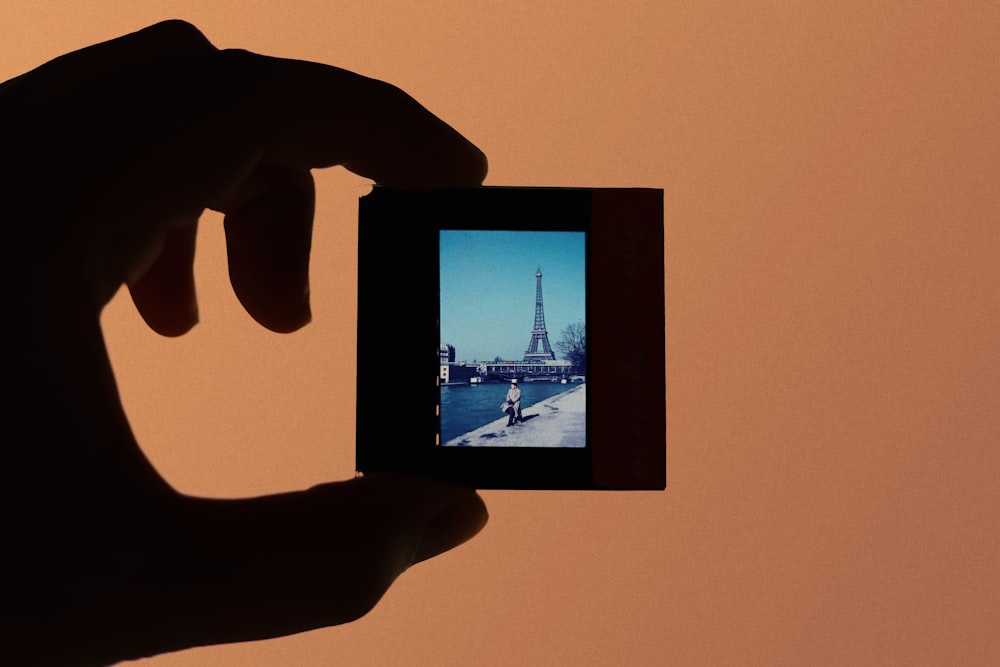 a person holding up a small camera to take a picture of the eiffel