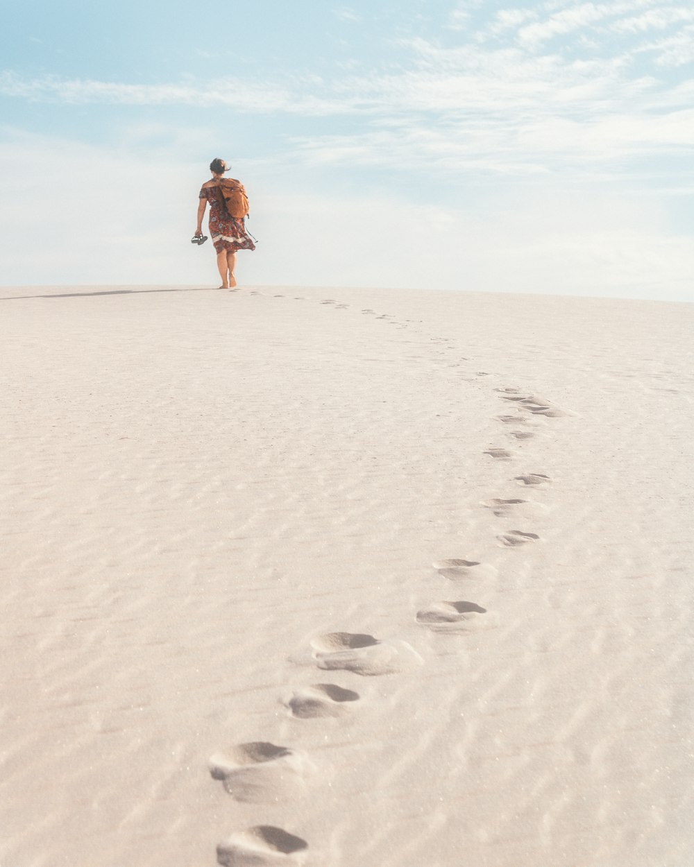 a man walking across a sandy beach with footprints in the sand
