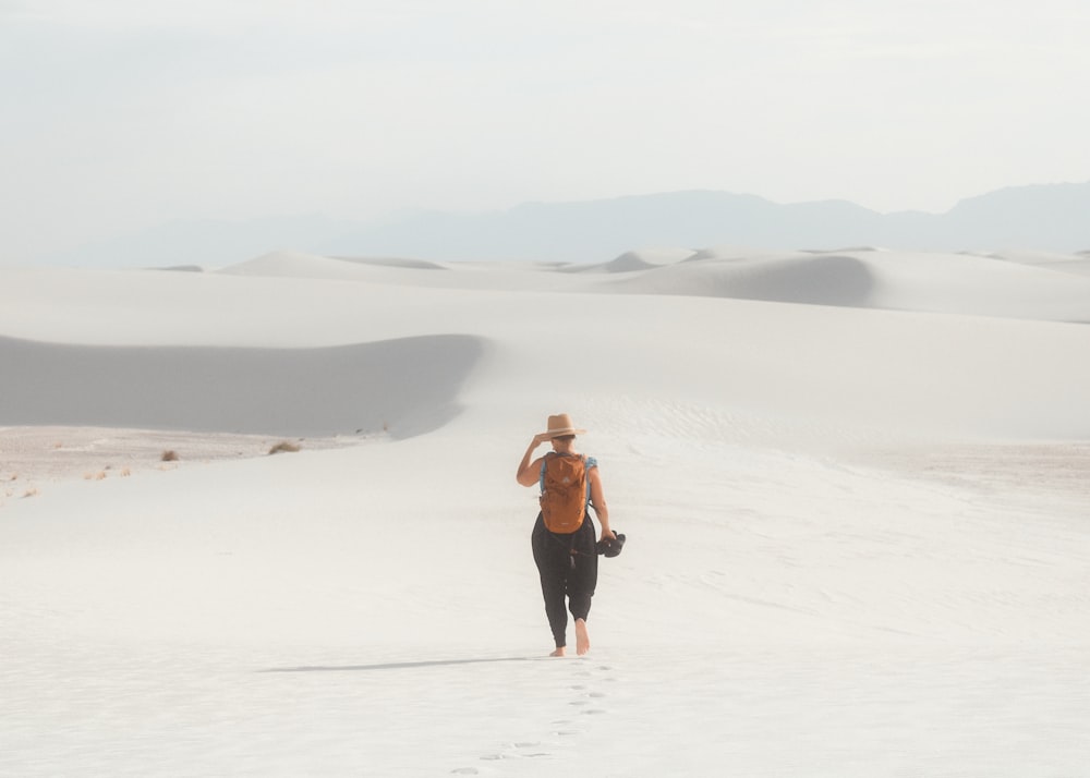 a woman walking across a white sand dune