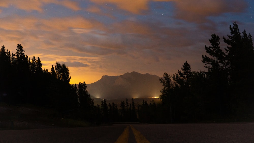 a long road with trees and mountains in the background