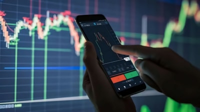 a person holding a cell phone in front of a stock chart