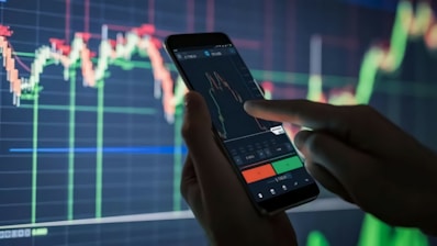 a person holding a cell phone in front of a stock chart